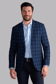 A man with dark hair and a beard wears Twillory's AIR Blazer in Navy Blue Plaid over a light blue dress shirt and dark trousers, standing against a plain light gray background with a relaxed posture and slight smile.
