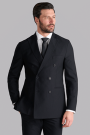 A man with a trimmed beard and combed dark hair wears the Twillory AIR Double Breasted Blazer // Black, crafted from 360° Airflow Fabric. He stands with one hand in his pocket, looking left against a plain light gray background.