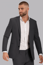 A man with short hair and a beard wears the Twillory AIR Blazer in Charcoal over a white shirt. He faces left with a neutral expression, jacket unbuttoned and left hand slightly raised, set against a light grey background.