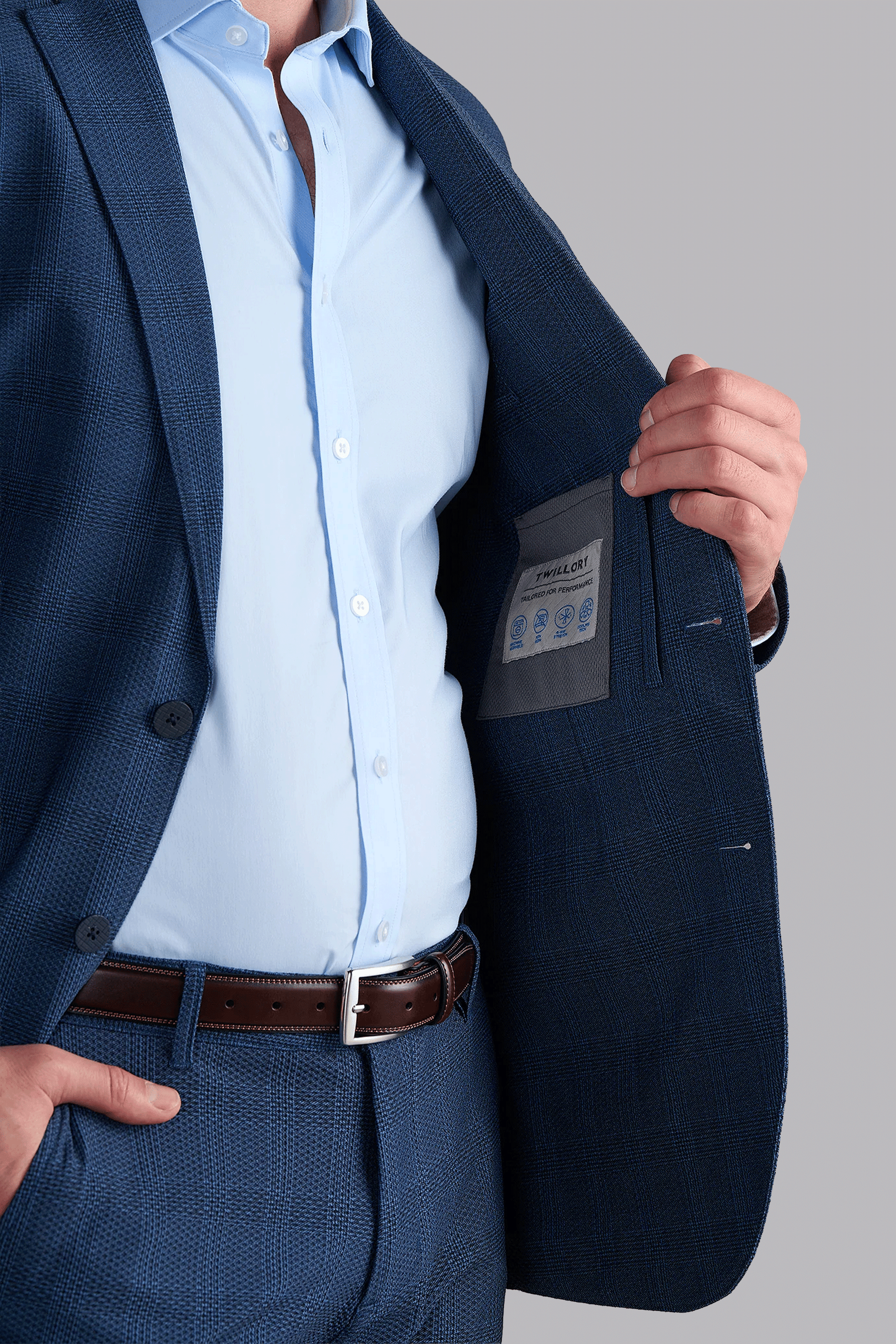 A man in a blue AIR Blazer // Blue Prince of Wales suit and light blue shirt holds open his jacket to reveal the 360° Airflow Fabric and fabric care label inside; his face is not visible.