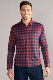 A smiling man faces forward in Twillory’s Long Sleeve Button Down Polo Gingham in Red Blue, paired with dark pants. The plain, light background highlights his outfit.