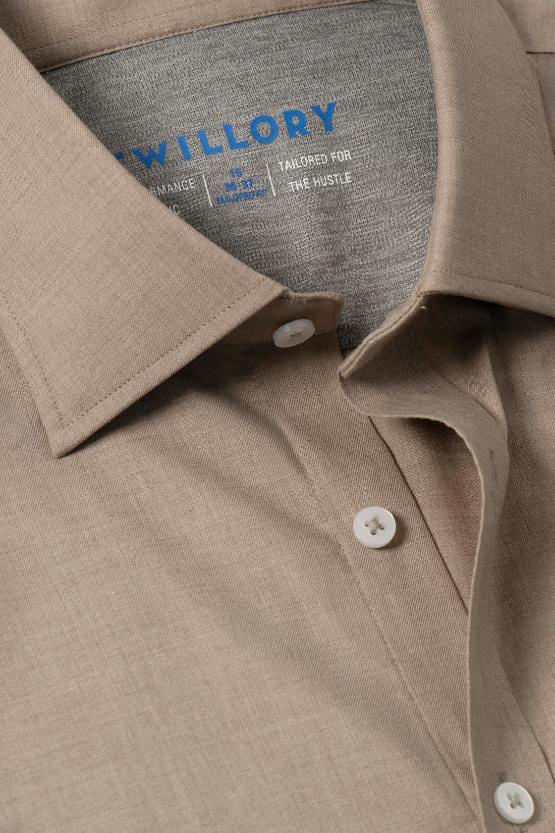 A close-up of the Leader Solid // Heather Sepia shirt by Twillory shows white buttons and a blue brand label on the inner collar. Made from smooth, finely woven fabric, this button-up offers 4-way stretch and subtle moisture wicking.