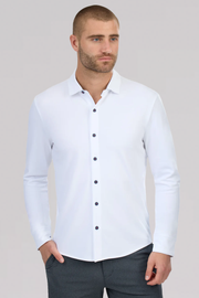 A man with short hair and a beard models the Twillory Long Sleeve Button Down Polo Contrast in White Navy Stitch, featuring dark buttons. He stands sideways with one hand in his pocket against a light gray background.