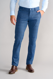 A person wears Twillory Performance Pants // BLUE PRINCE OF WALES with a shirt-gripping waistband, paired with a light blue dress shirt and brown leather shoes. One hand is in their pocket. The plain light background and head are not visible.