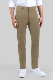 A man stands against a gray background in Twillory’s Performance Five Pocket // KHAKI pants—featuring subtle 4-way stretch—styled with a white non-iron shirt (sleeves rolled) and white sneakers for a neat, casual look.