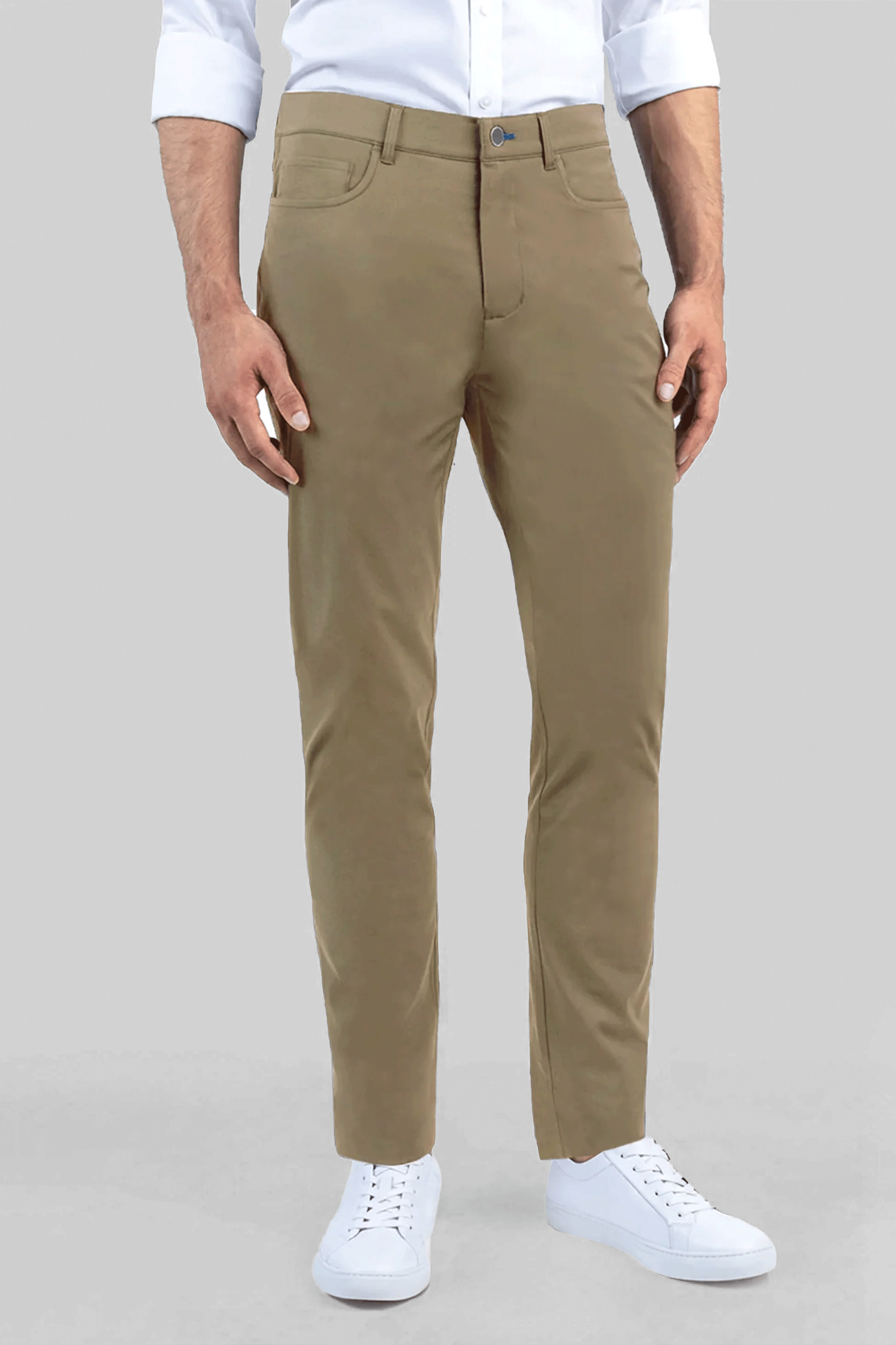 A man stands against a gray background in Twillory’s Performance Five Pocket // KHAKI pants—featuring subtle 4-way stretch—styled with a white non-iron shirt (sleeves rolled) and white sneakers for a neat, casual look.
