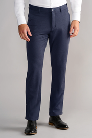 A person wears Twillory Circular Knit Pants in Heather Navy paired with a tucked-in white shirt and black leather dress shoes, standing against a plain light gray background. Only the lower torso and legs are visible.