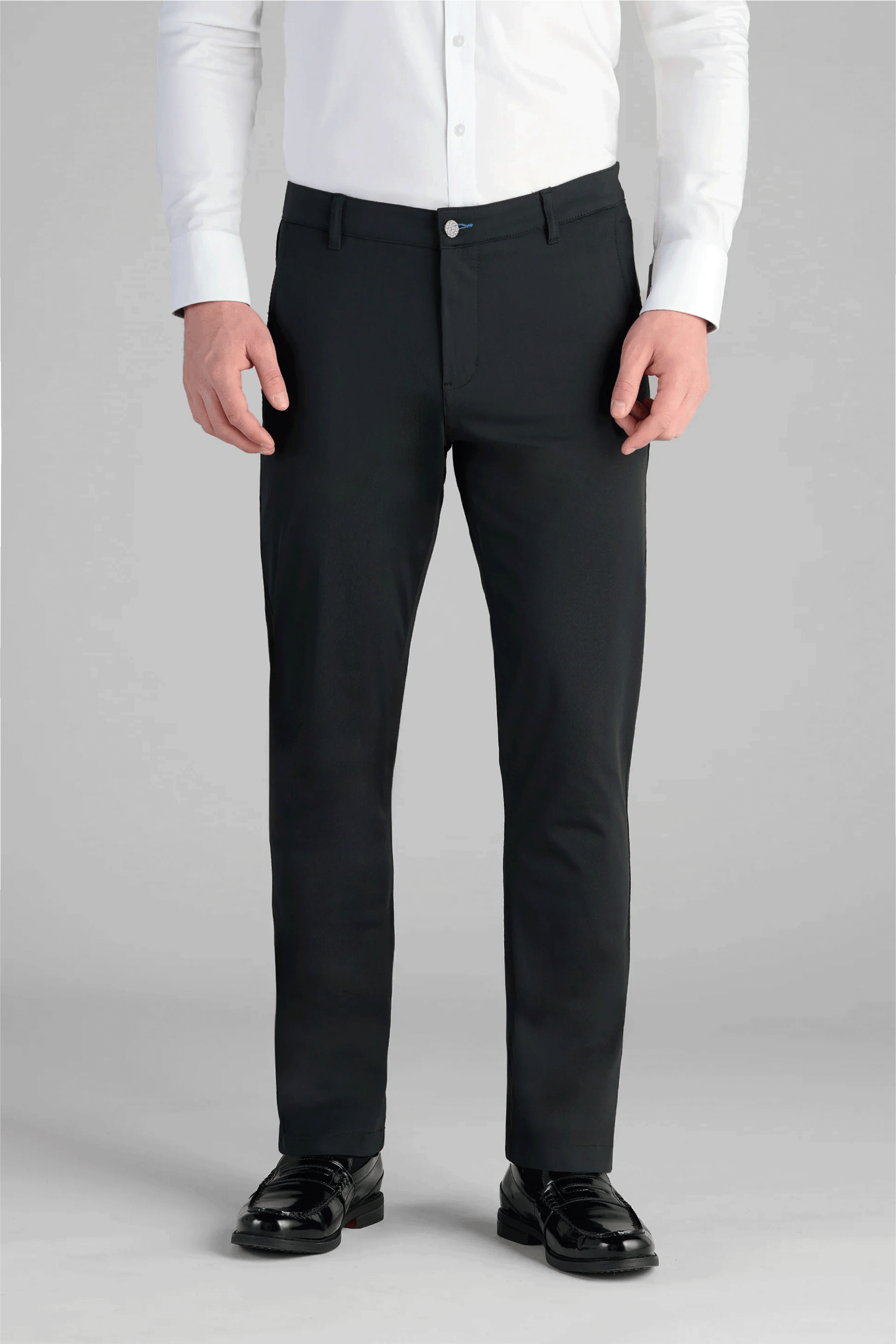A person models the Performance Pants // BLACK with a white button-up shirt and black dress shoes, standing against a plain gray background. The photo is taken from shoulders to feet.