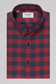 The Twillory untuck(able) Barnyard Gingham is a long-sleeve button-up shirt in red and navy plaid, featuring a structured collar, black buttons, and non-iron stretch fabric for smart casual comfort. Displayed on light gray.