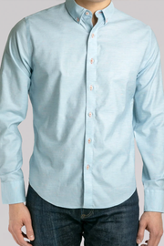 A man wears the Twillory untuck(able) Caribbean Melange—a light blue, smart casual, non-iron stretch button-down shirt—neatly pressed and paired with dark blue jeans, highlighting its upper torso fit and untuckable style.