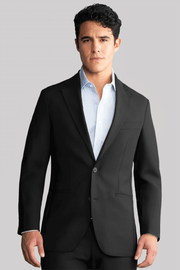 A young man with short, curly dark hair wears the Twillory Hybrid Wool Blazer in Black over a light blue dress shirt, standing forward with a neutral expression against a plain light gray background.