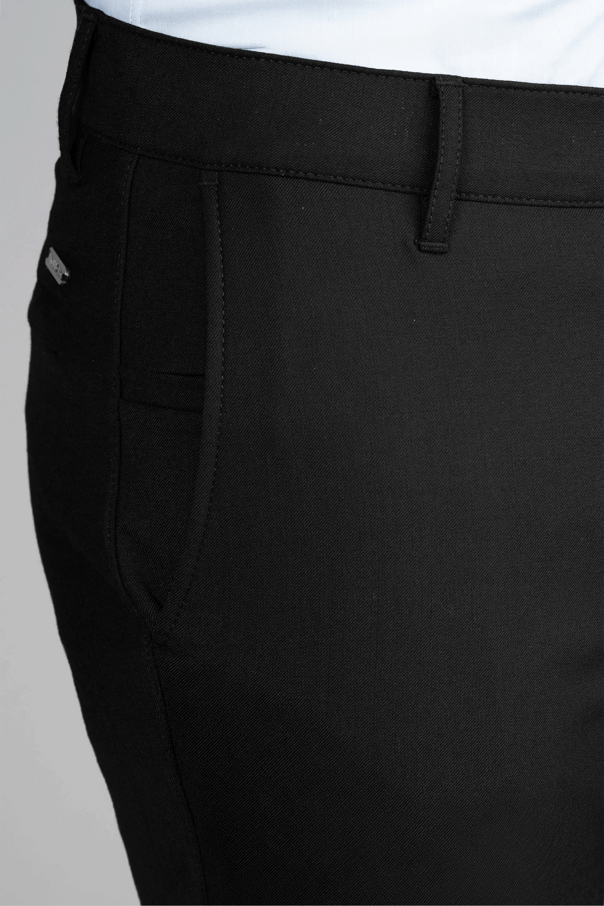 Close-up of a person wearing Twillory Hybrid Wool Pants // Black and a white shirt, focusing on the left hip with the side pocket, 4-way stretch fabric, silver logo pin above the pocket, and detailed stitching.