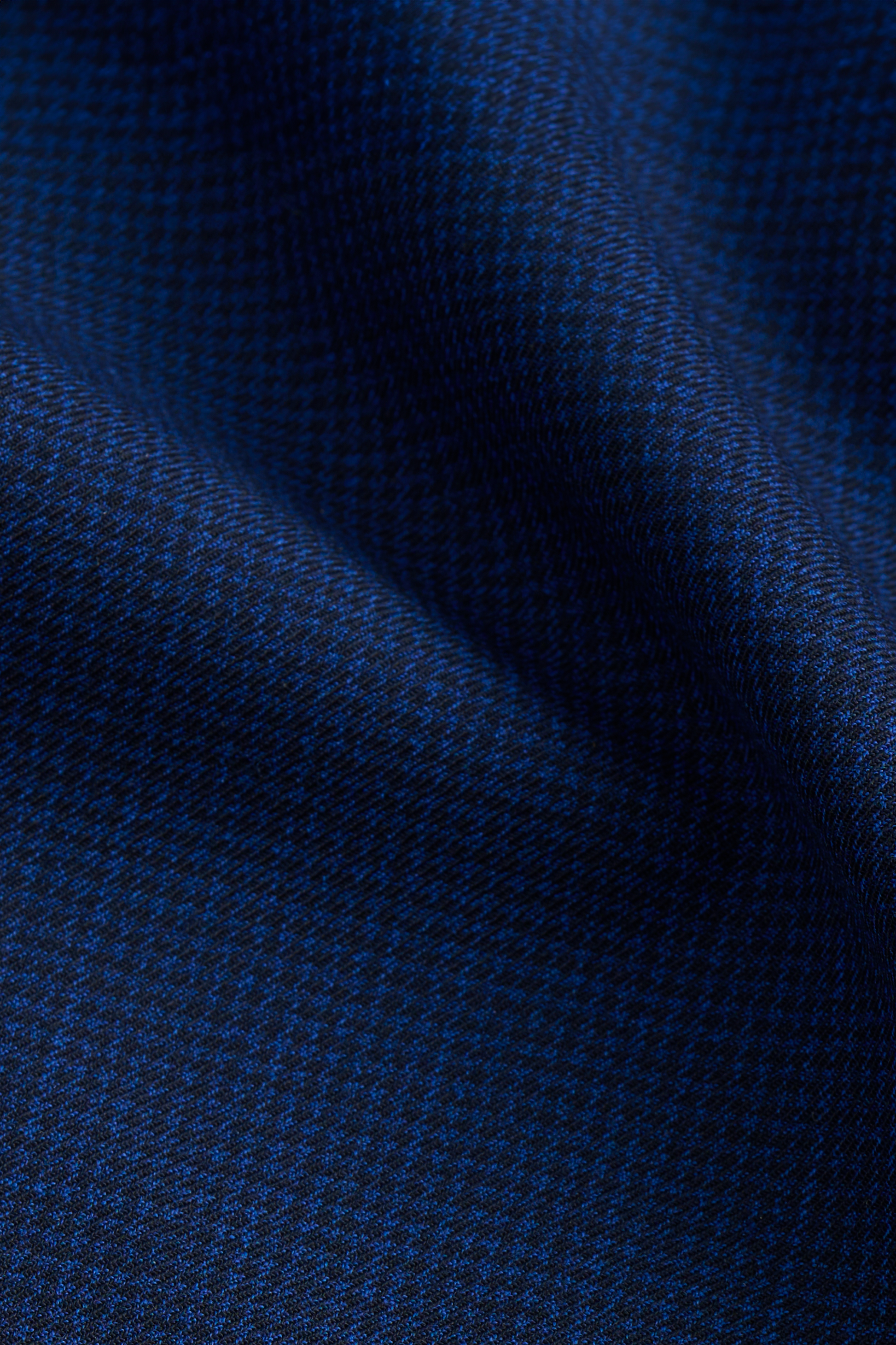 Close-up of Twillory's Hybrid Wool Blazer // Navy Puppytooth shows the dark blue, machine washable fabric with a subtle textured pattern and light blue threads. Its 4-way stretch and soft sheen highlight the blazer’s refined, modern style.