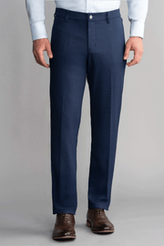 A person wears Twillory Hybrid Wool Pants in Navy Puppytooth, featuring a tailored fit and 4-way stretch, with a light blue dress shirt tucked in. Brown leather dress shoes complete the look against a plain light gray background.