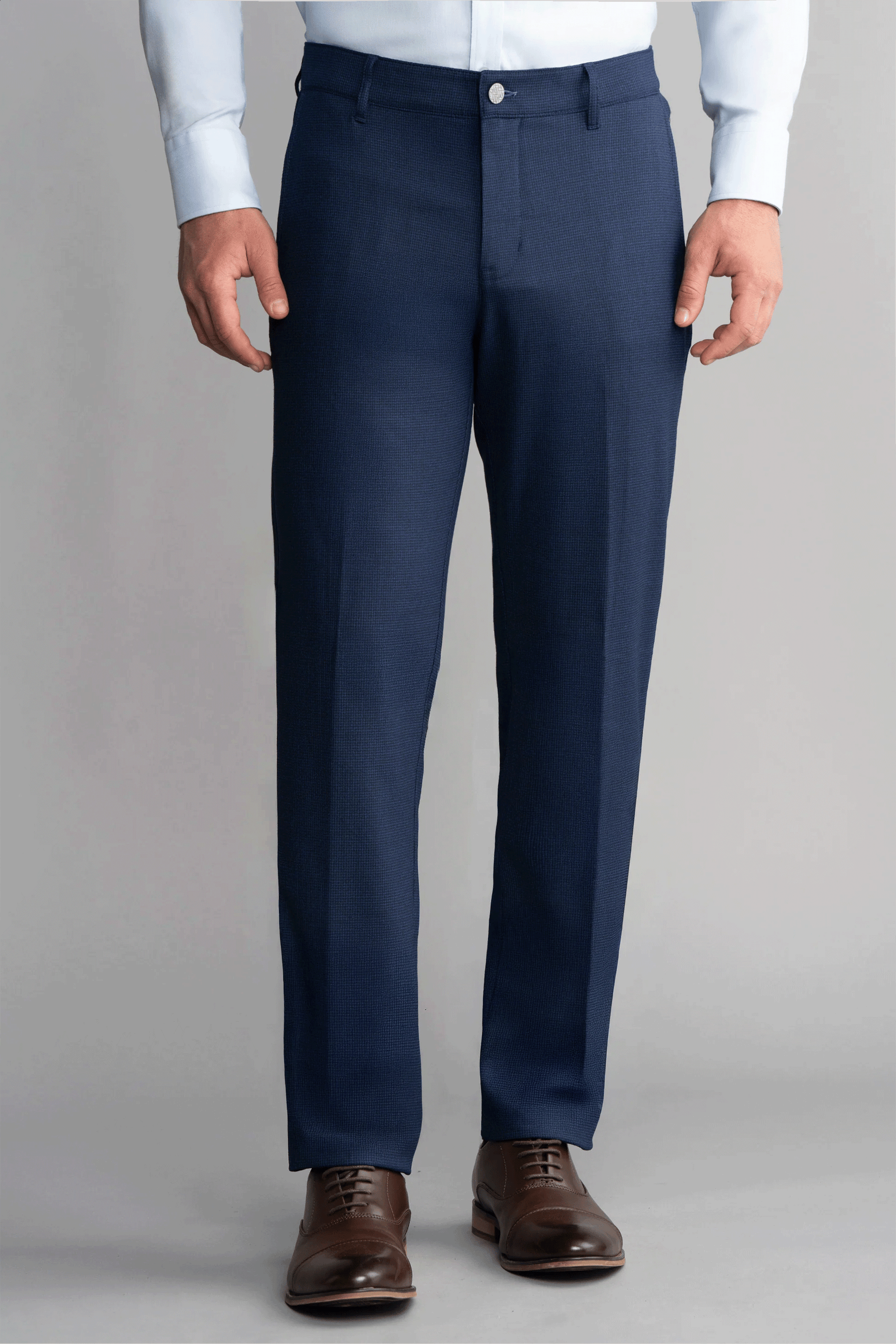 A person wears Twillory Hybrid Wool Pants in Navy Puppytooth, featuring a tailored fit and 4-way stretch, with a light blue dress shirt tucked in. Brown leather dress shoes complete the look against a plain light gray background.