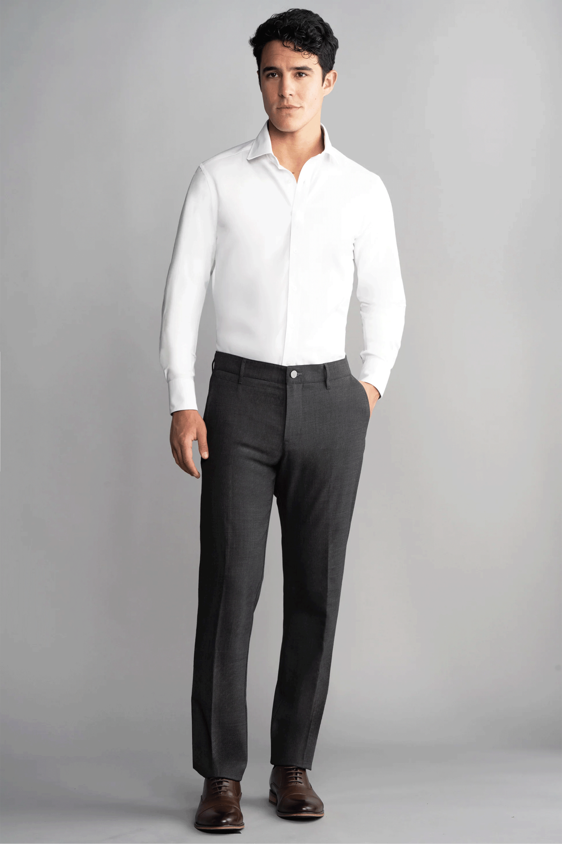 A man stands against a plain gray background, wearing the Twillory Hybrid Wool Blazer in Grey Heather. With neat hair and brown dress shoes, he faces forward, his look blending style and comfort for modern versatility.