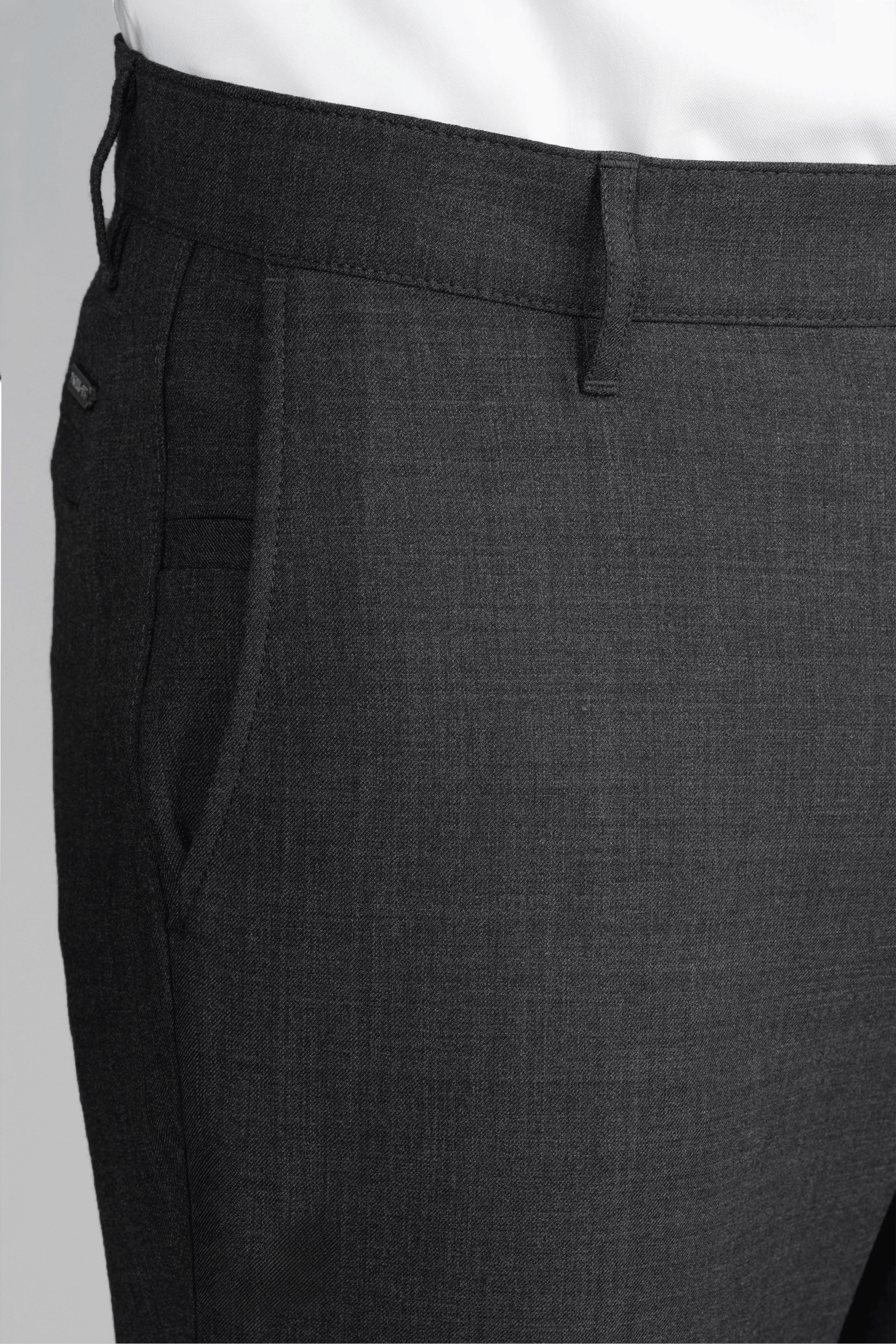 Close-up of Twillory Hybrid Wool Pants in Grey Heather featuring a subtle textured pattern, 4-way stretch, belt loops, and front pockets. Shown with a tucked-in white shirt; only the waist and upper legs are visible against a plain background.