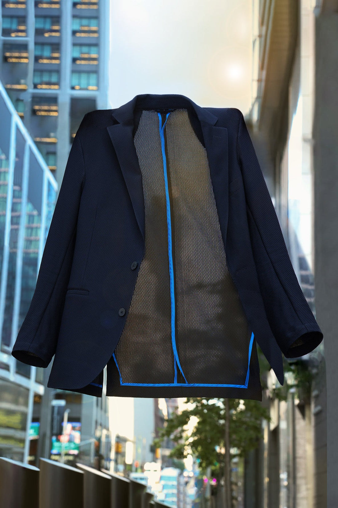 Black mesh unisex blazer jacket floating in mid-air on urban street background with high-rise buildings.