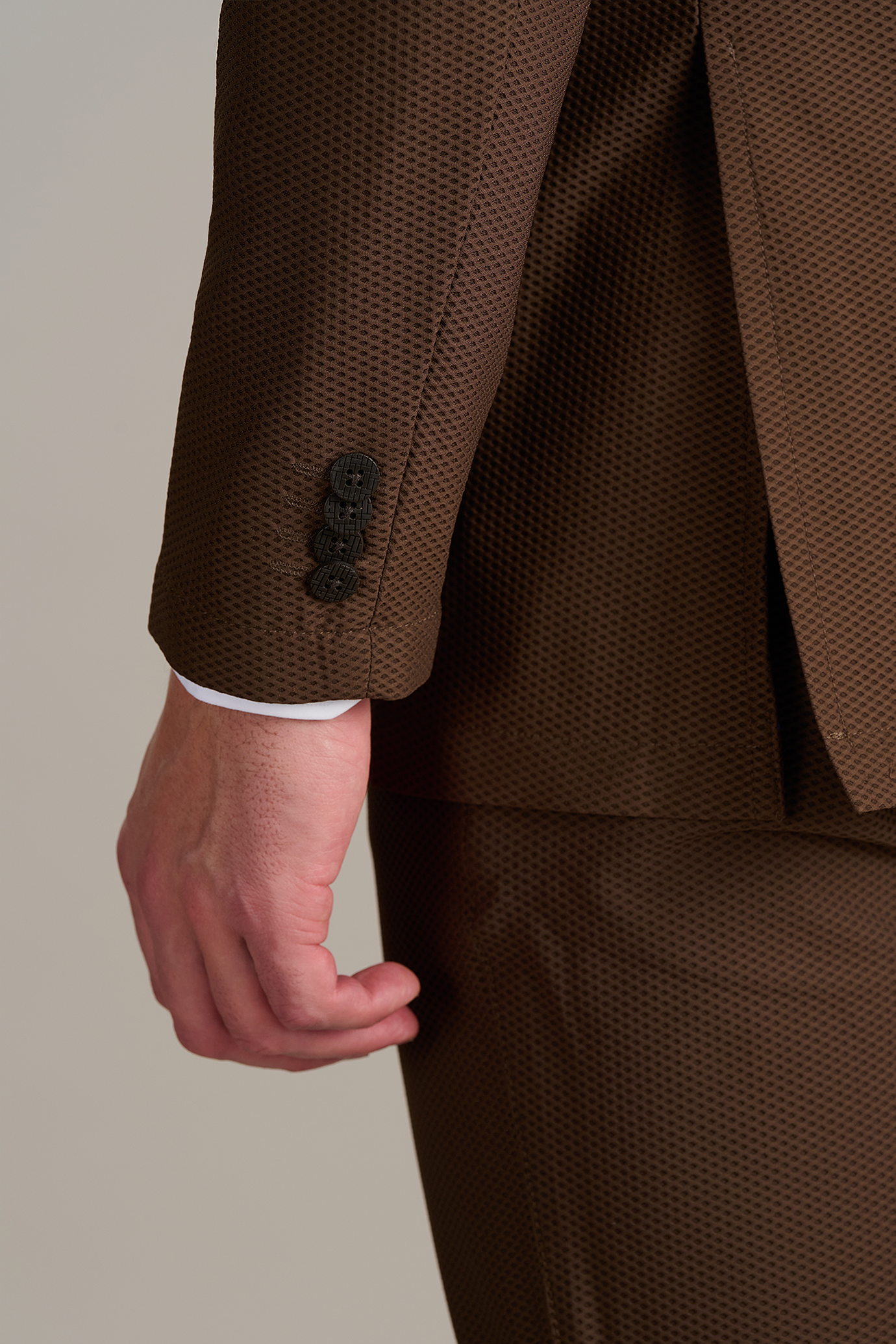 Close-up of a person's arm in a textured brown suit with black buttons, highlighting the sleeve detail and tailored fit.