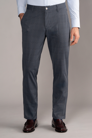 A man wears Twillory’s Performance Pants in Grey Prince of Wales, paired with a tucked-in light blue dress shirt and dark brown loafers. His hands are in his pockets, chest down visible, standing against a neutral background.