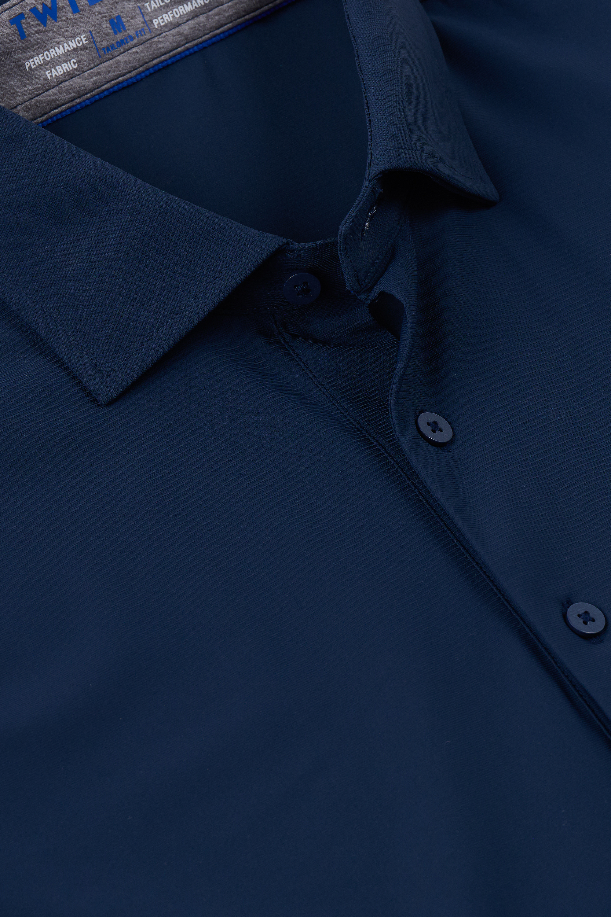 Close-up of the Twillory Event Polo Solid in Navy. The smooth, slightly shiny fabric is wrinkle-free with performance stretch. Features a pointed collar, two blue buttons on the placket, and a label inside the collar with blue and white text.