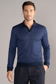 A man with short brown hair and a trimmed beard wears Twillory's Long Sleeve Sweater Polo Solid in navy, featuring dark cuffs and a V-neck Johnny collar, standing against a grey background with one hand in his trouser pocket.