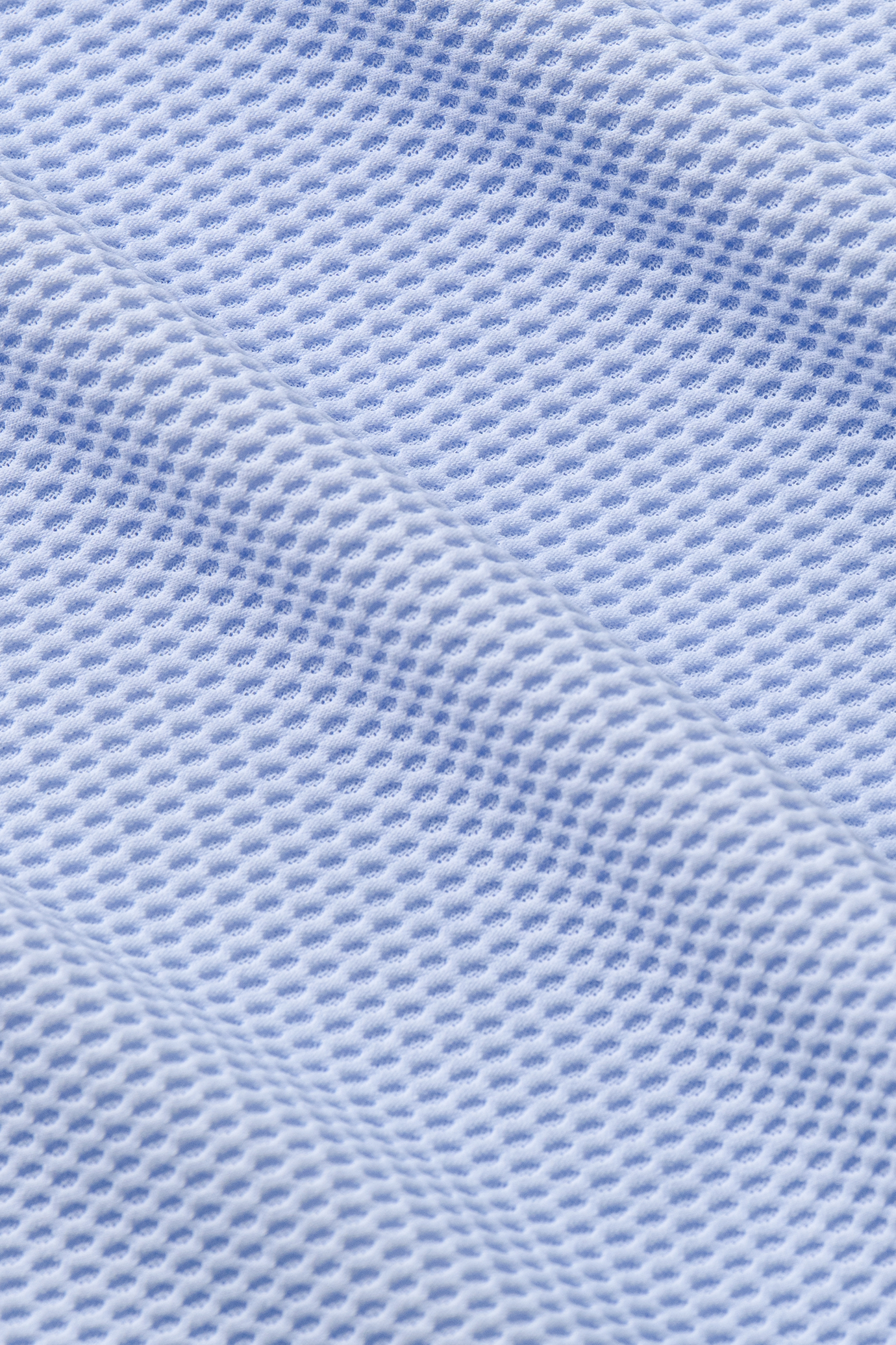 A close-up of the AIR Resort Shirt Solid in Powder Blue by Twillory reveals cooling mesh fabric with evenly spaced holes, showcasing breathability—ideal for a machine washable, comfortable button-down. Soft shadows hint at its gentle folds and sleek lines.