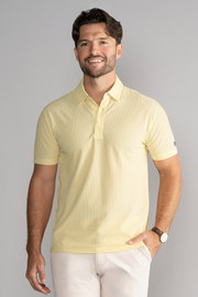 A man with short brown hair and a trimmed beard smiles as he models the Twillory AIR 3 Button Polo Solid in yellow, paired with light-colored pants and a watch, standing against a plain gray background with one hand in his pocket.