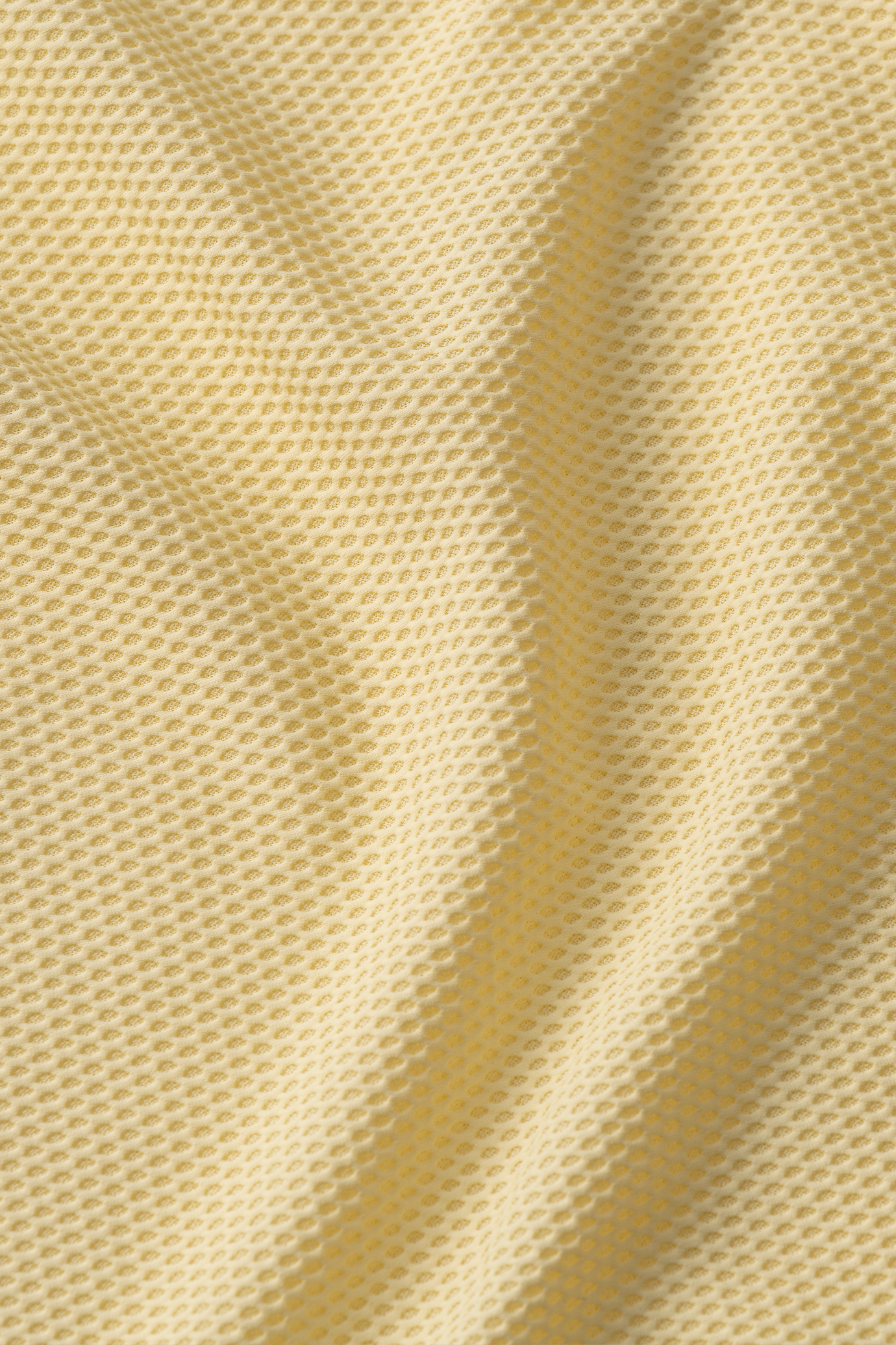Close-up of Twillory's AIR Zip Polo Solid // Yellow: light yellow, soft 360° Airflow Fabric features a small hexagonal mesh pattern. Gentle folds and texture highlight the hyper-breathable, flexible material.