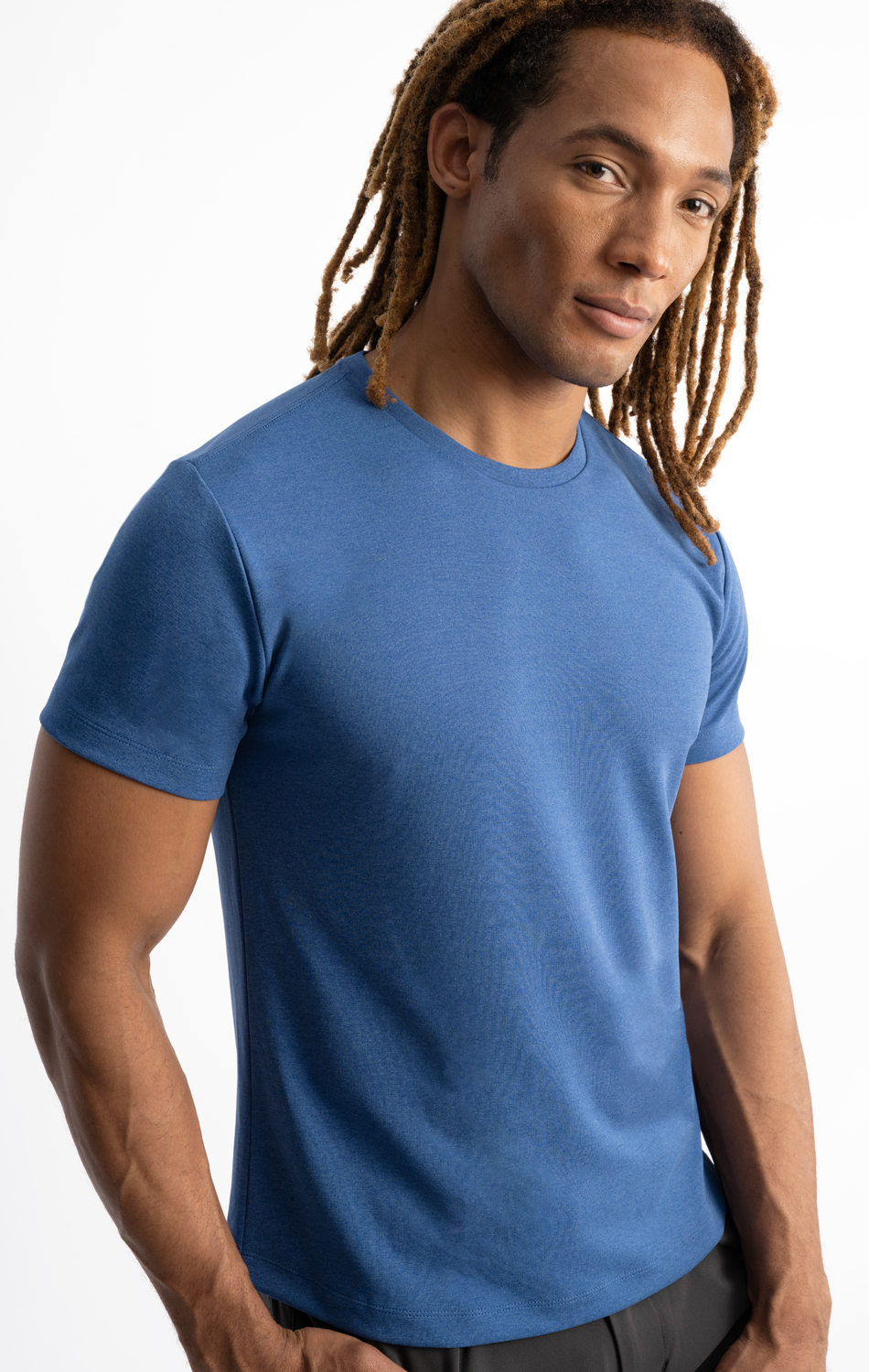 Man wearing a blue t-shirt with dreadlocks, standing in a relaxed pose against a white background.