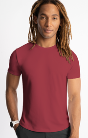 Man wearing a red t-shirt with long dreadlocks and a white wristwatch, standing against a white background.