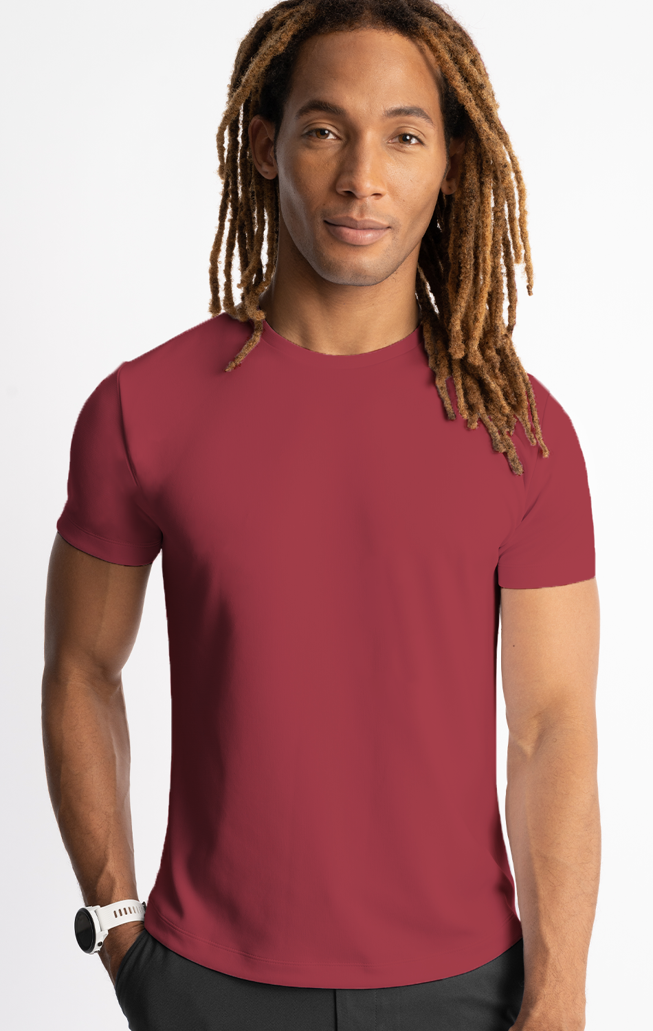 Man wearing a red t-shirt with long dreadlocks and a white wristwatch, standing against a white background.