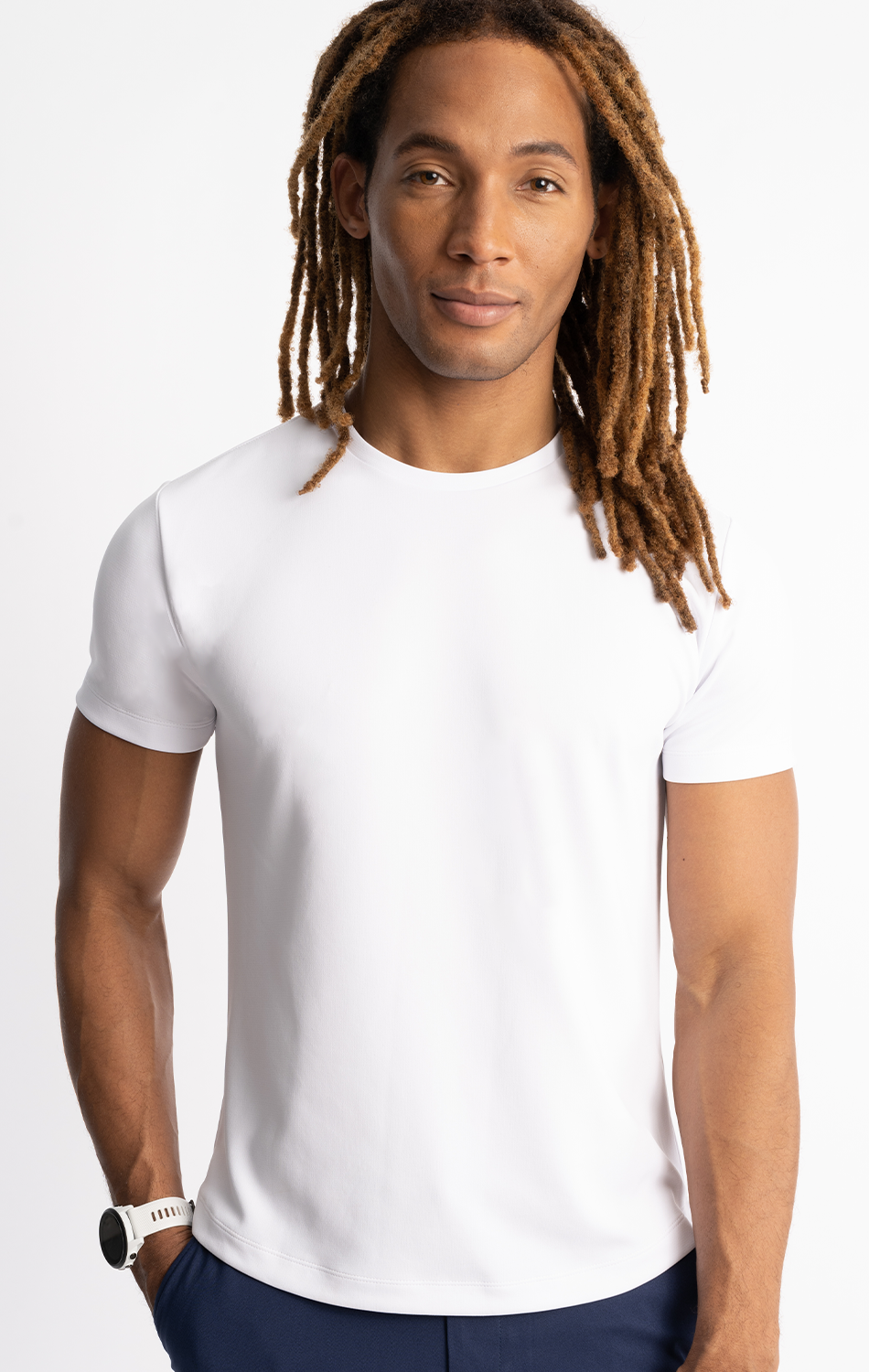Man with long hair wearing a white t-shirt and wristwatch standing against a plain background.
